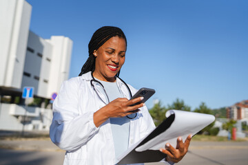 african american woman doctor hold cellphone and scan document outdoor