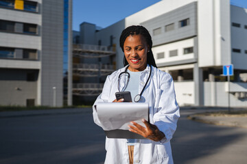 african american woman doctor hold cellphone and scan document outdoor