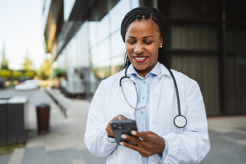 african american woman doctor on break use cellphone in front hospital