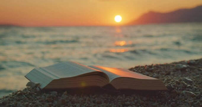 Open book rests on pebbles as sun sets over ocean in serene landscape of Croatia