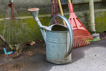 Vintage metal watering can and red rake arranged together on concrete patio in garden setting