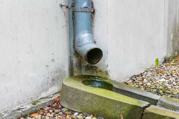 Metal drainage pipe with water flowing onto gravel surface creating urban infrastructure detail