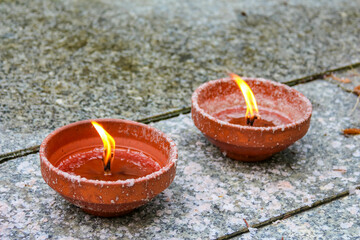 Two clay oil lamps with glowing flames positioned on weathered stone creating peaceful meditation...