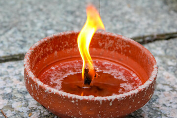 Clay oil lamp with tall bright flame creating dramatic lighting effect on stone surface