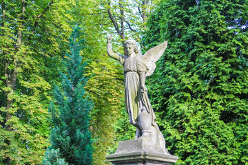Angel statue with outstretched wings positioned in peaceful garden setting surrounded by greenery