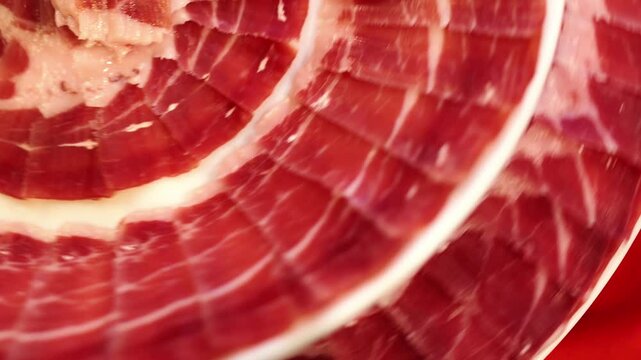 Slices of serrano ham, arranged in a circular pattern, rotate slowly, showcasing their rich color and texture