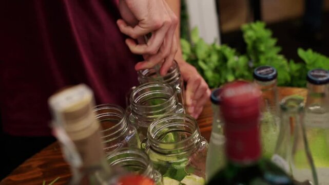 Bartender muddling mint and lime in glass jars, preparing a batch of mojitos for a party or event