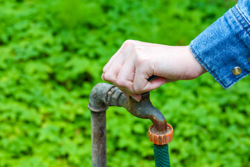 Close-up of hand operating ornate vintage cemetery water faucet showing detailed metalwork...