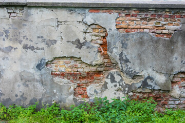 Crumbling brick wall with damaged plaster revealing layered weathering patterns and structural...