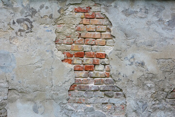 Weathered brick wall with exposed patches showing natural decay patterns and aging texture in...