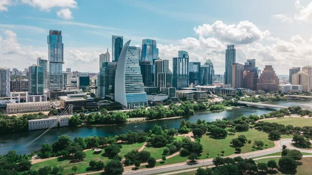 Drone hyperlapse orbits Auditorium Shores, smoothly panning across Austin Texas skyline and Ladybird Lake. Busy summer morning scene with vibrant urban life, water reflections blue skies with clouds