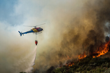 Helicopter tackles forest fire in mountainous area during daytime as smoke billows into the sky