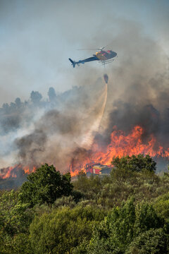 Helicopter tackles forest fire in mountainous area during daytime as smoke billows into the sky