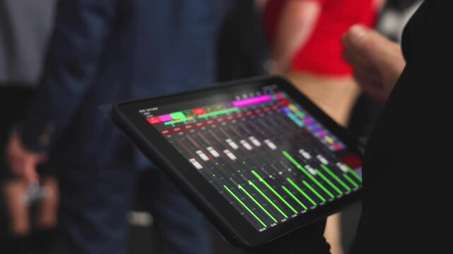 View of lighting technician with tablet, operator controlling sound and light during live event concert on stage show broadcast, staff personnel with professional equipment, working on mixing console