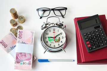 Turkish Lira Banknotes designed on white surface with calculator,glasses,agenda and vintage alarm clock	