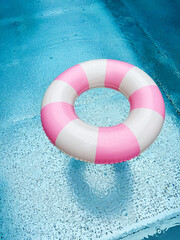 Swimming ring with pink and white stripes in a blue outdoor pool. Poolside atmosphere. Pink float.