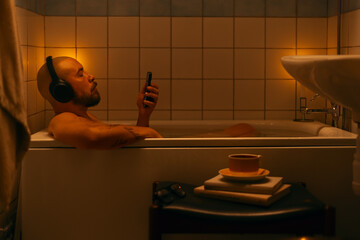 Handsome man in wireless headphones relaxing in bath and enjoying music