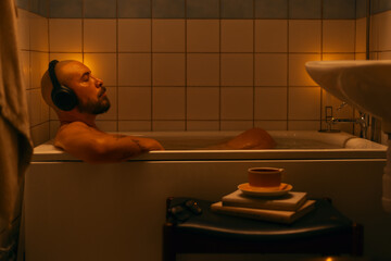 Handsome man in wireless headphones relaxing in bath and enjoying music