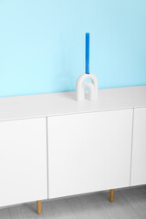 Wooden chest of drawers with candle near blue wall in room