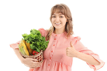 Happy young female farmer with wicker basket full of different ripe vegetables showing thumb-up...