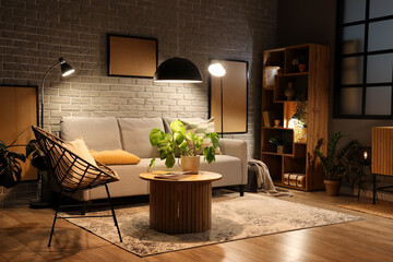 Interior of modern living room with grey sofa, wooden coffee table and glowing lamps at evening