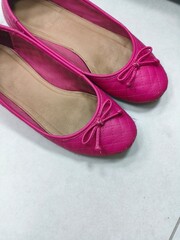 Pink quilted ballet flats with bows on white tiled floor, used women’s shoes showing signs of wear, casual feminine fashion footwear for everyday or indoor use