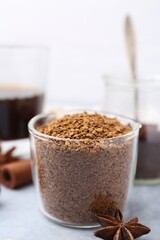 Granulated instant coffee in measuring cup and spices on grey table against light background, closeup