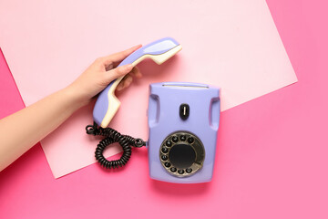 Female hand with lilac retro telephone on pink background