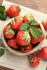 Fresh ripe strawberries and leaves in bowl on wooden table, flat lay