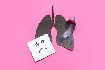 Black paper lungs, ribbon and note with sad face on pink background