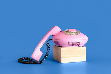 Wooden podium with pink retro telephone on blue background