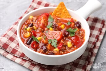 Tasty chili con carne in bowl and nachos on grey textured table, closeup