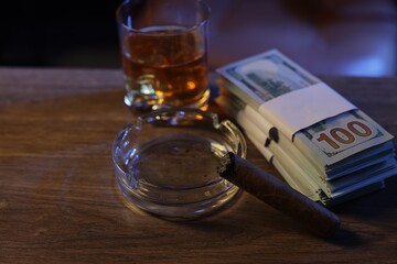Mafia and criminal world. Ashtray with cigar, money and whiskey on wooden table, closeup