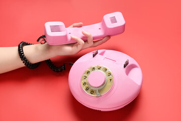 Female hand with pink retro telephone on red background
