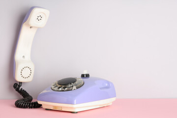 Lilac retro telephone on pink table against white background