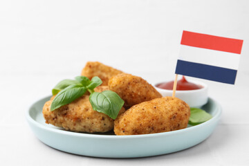 Tasty fried croquettes, basil, sauce and flag of Netherlands on white tiled table, closeup