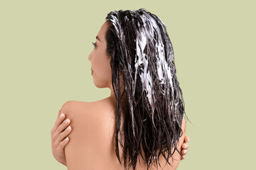 Young woman with hair mask on green background, back view