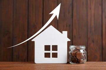 Increase in real estate value. House model and jar of coins on wooden background. Growing price...