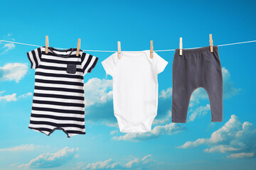 Different baby clothes drying on washing line against blue sky