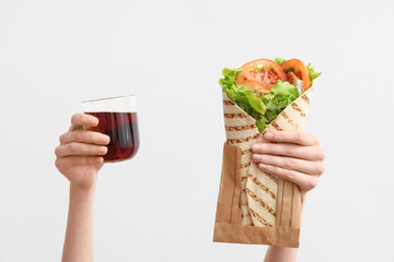 Hands with tasty doner kebab and drink on light background
