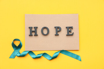 Teal ribbon and paper with word HOPE on yellow background. Sexual Assault Awareness Month