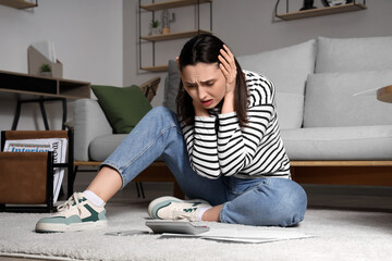Depressed young woman with calculator and papers at home