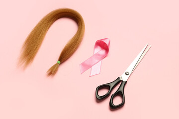 Red hair strand for donation with awareness ribbon and scissors on pink background