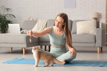 Young woman playing with cute kitten on yoga mat at home © Pixel-Shot