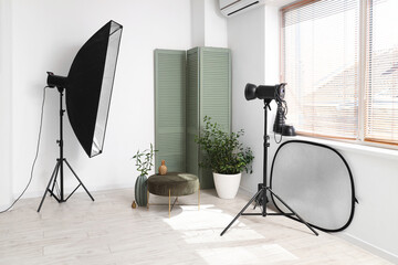 Interior of photo studio with professional equipment, folding screen, pouf and houseplant