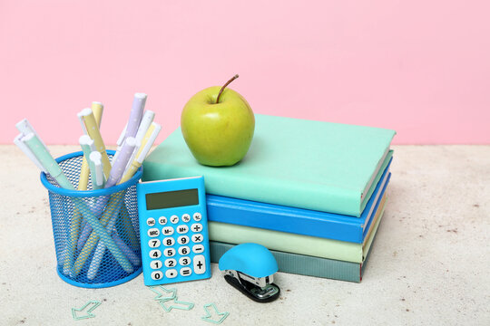Calculator, stapler, different school supplies and green apple on table against pink background - Powered by Adobe