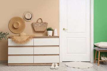Chest of drawers with straw hat, wicker bag and houseplant in hallway