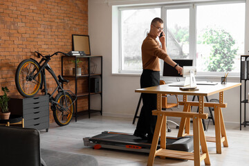 Young businessman talking by mobile phone on treadmill at table in office