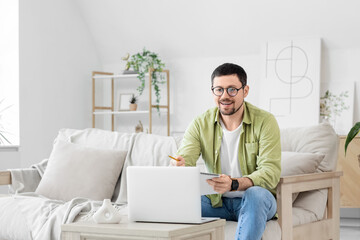 Young male teacher with laptop and notebook giving online lesson at home