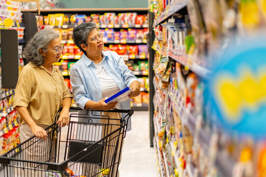 Happy Asian senior woman shopping buying food and grocery at supermarket. Elderly women friends enjoy healthy lifestyle reading label, choosing organic safety food, vegetable and groceries on shelf. - Powered by Adobe